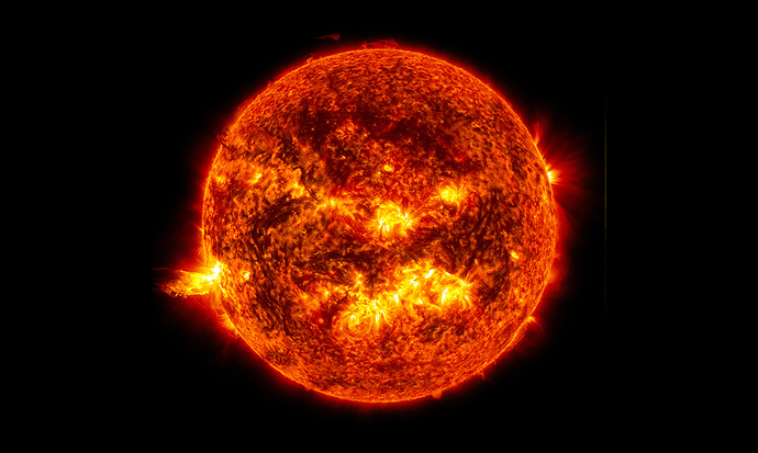 This image shows the bright light of a solar flare on the left side of the Sun and an eruption of solar material shooting through the Sun's atmosphere.